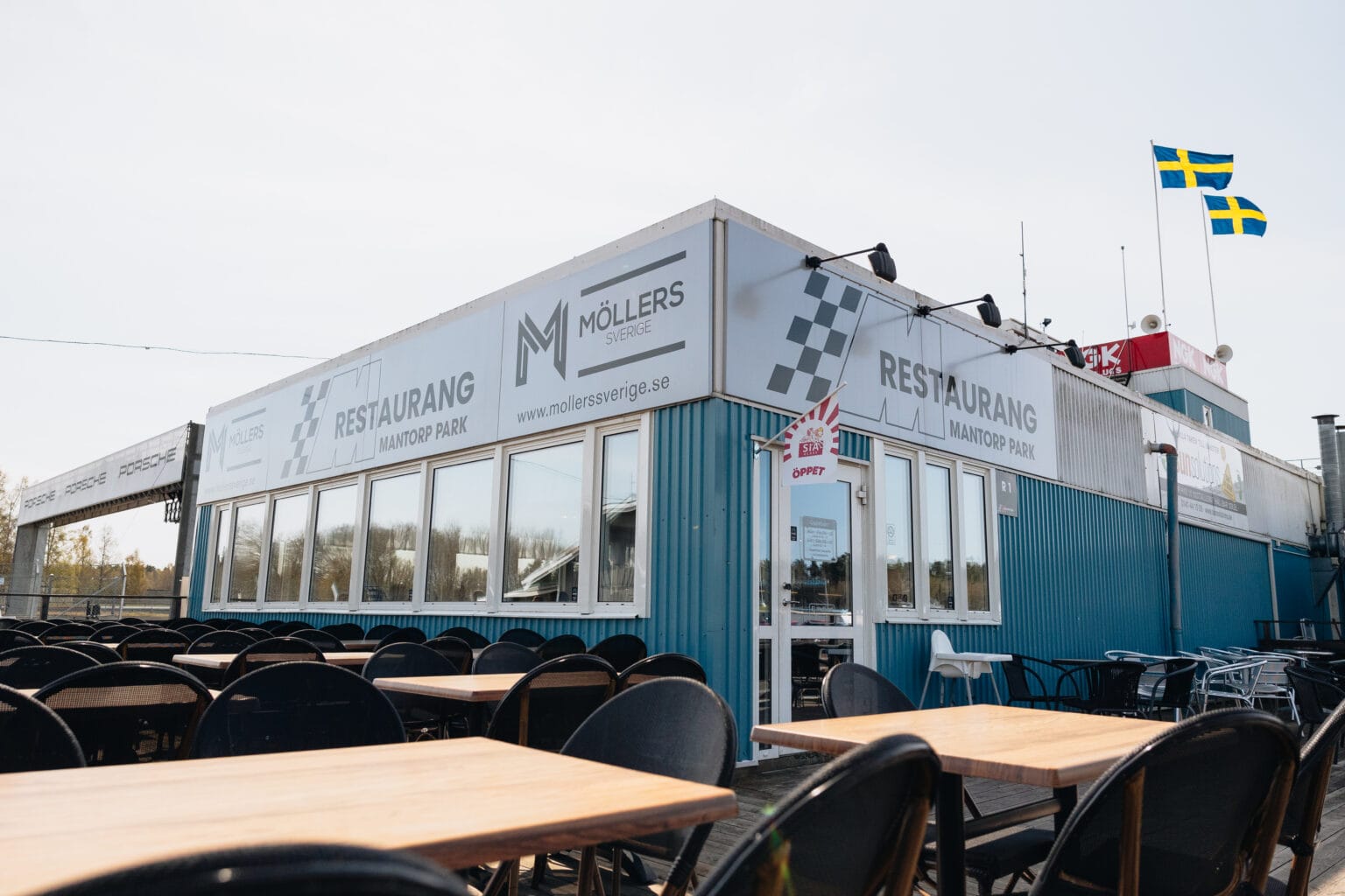 En blåvit byggnad med Restaurang Möllers skylt, många tomma bord och stolar utomhus samt två svenska flaggor på taket, fotograferad en solig dag.