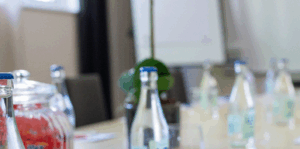 Ett konferensbord med vattenflaskor i glas, en burk med rött godis och ett tomt blädderblock i bakgrunden, vilket tyder på ett möte eller seminarium.