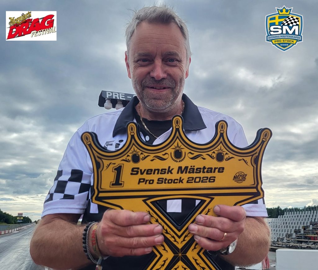En leende man i en rutig skjorta håller upp en stor guldfärgad skylt i form av en krona med texten ”1 Svensk Mästare Pro Stock 2026” på en racerbana. Logotyperna för Nordic Drag Festival och F-SM syns i hörnen.